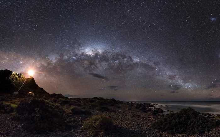 Milky Way over a rocky coastline with a lighthouse