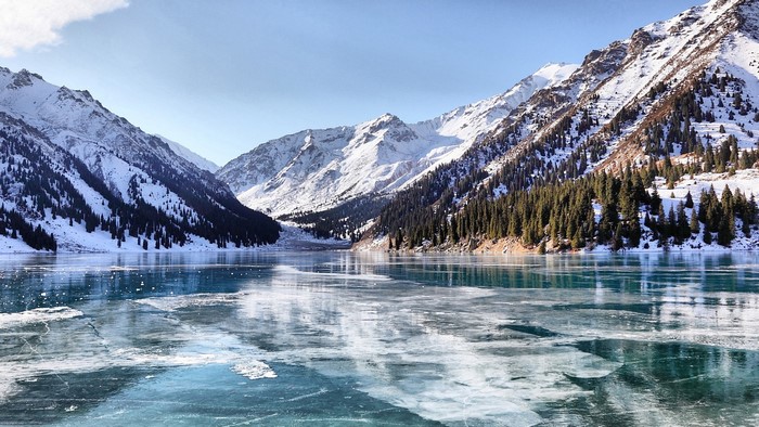 Frozen mountain lake with snow-capped peaks and pine forest