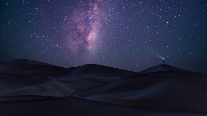 Person with flashlight under Milky Way in desert