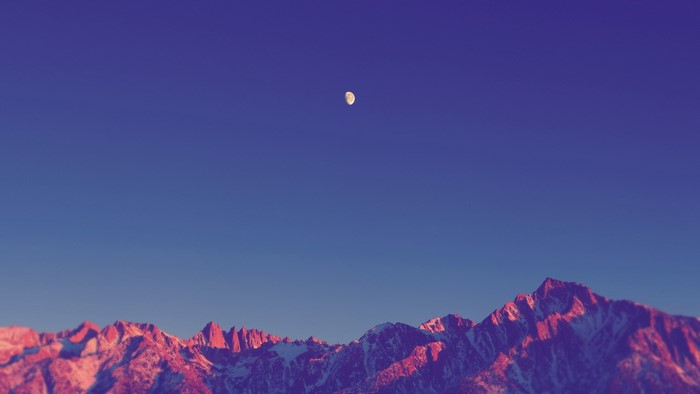 Moon over snow-capped mountains at sunset