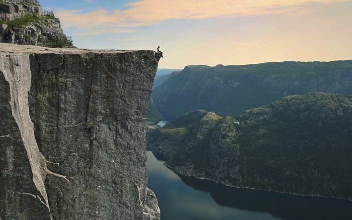 Person sitting on Preikestolen cliff overlooking Lysefjord, Norway