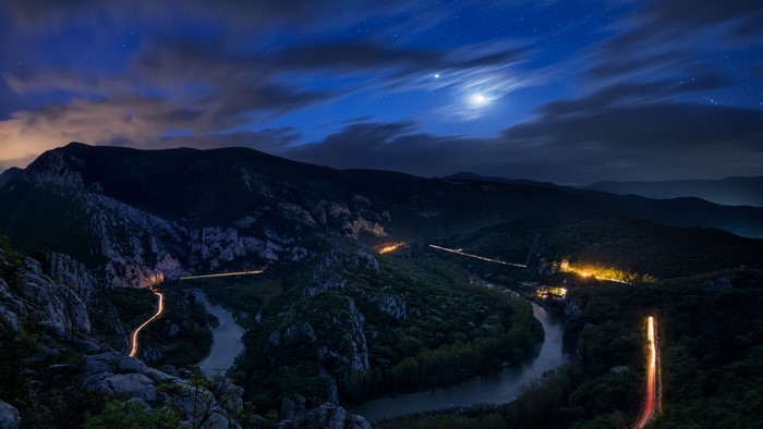 Night landscape with river, mountains, and light trails
