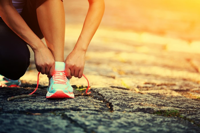 Person tying running shoe laces on asphalt path