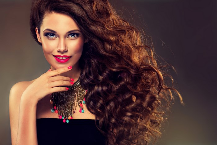 Woman with long curly brown hair and bright makeup