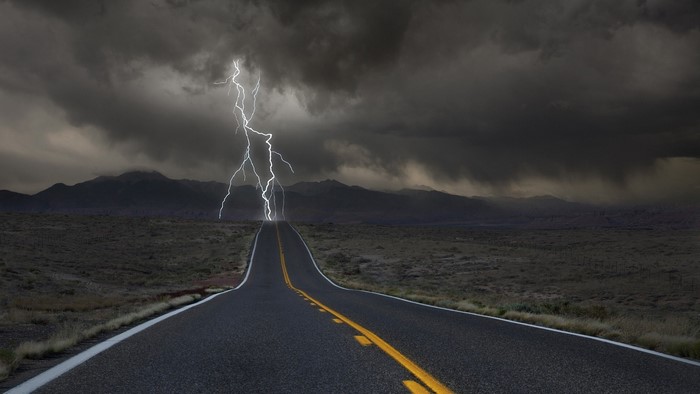 Lightning strikes over a desolate road and mountains