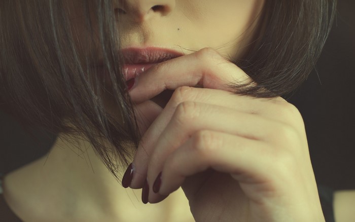Woman with dark hair and red nails biting lip