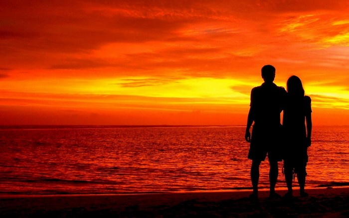 Couple silhouetted against a vibrant sunset over the ocean