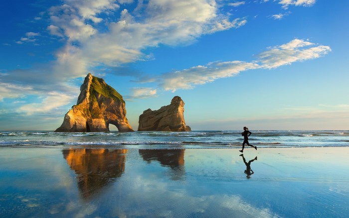 Person running on a beach with rock formations
