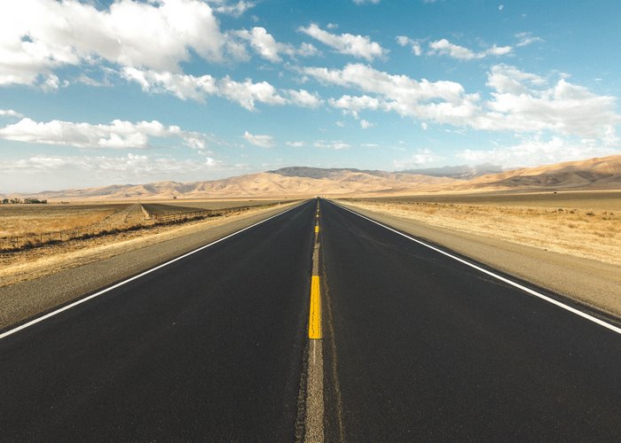 Desert road leading to mountains under a cloudy sky