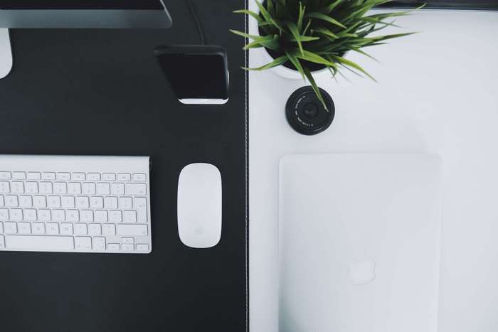 Apple keyboard, mouse, laptop, and plant on a desk