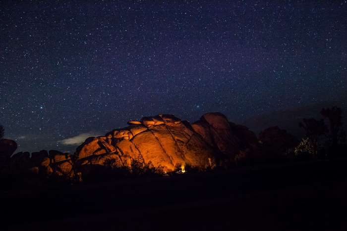 Campfire under starry sky near rocks 4K