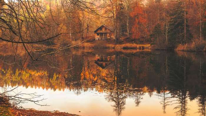 Cabin by a lake in autumn forest with reflections