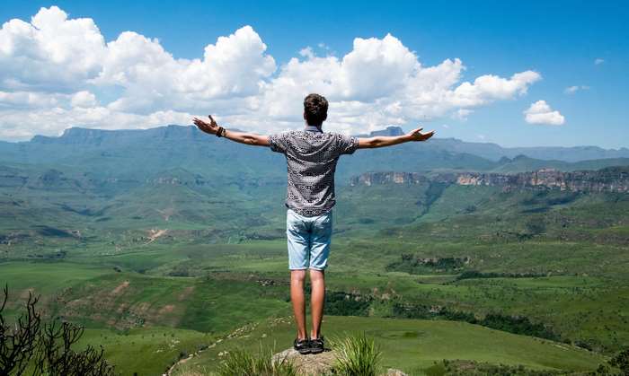 Man with arms outstretched on a mountain overlooking a valley