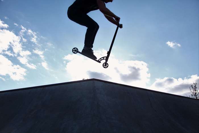Scooter rider jumping over ramp in park