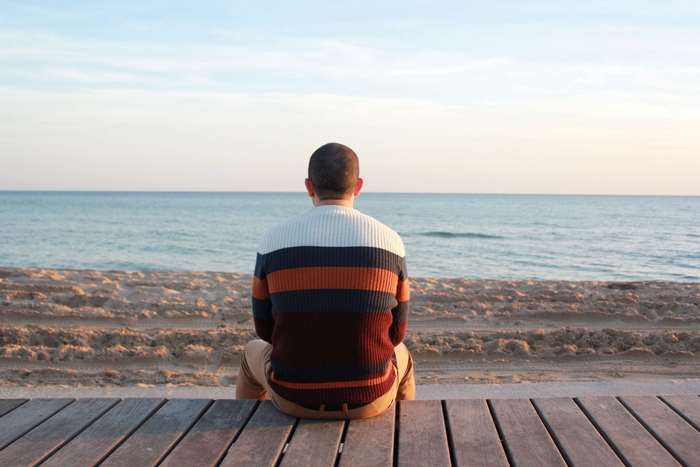 Man in striped sweater sitting on pier by the ocean