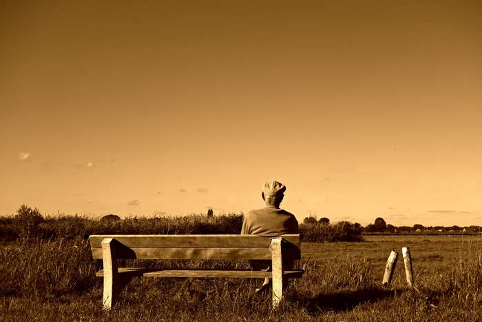 Elderly man sitting on a bench in a field