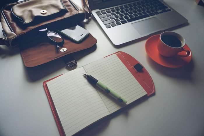 Desk with laptop, coffee, notebook, pen, bag, and smartphone