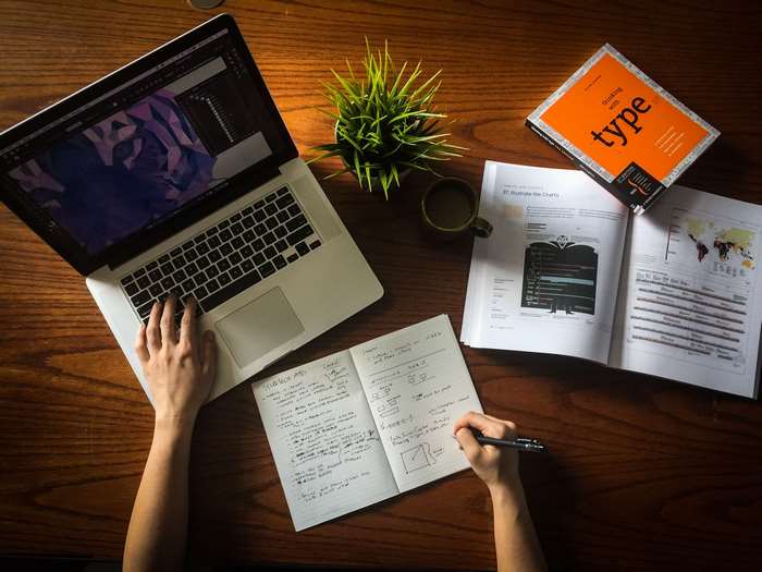 Person working on a laptop at a desk with books