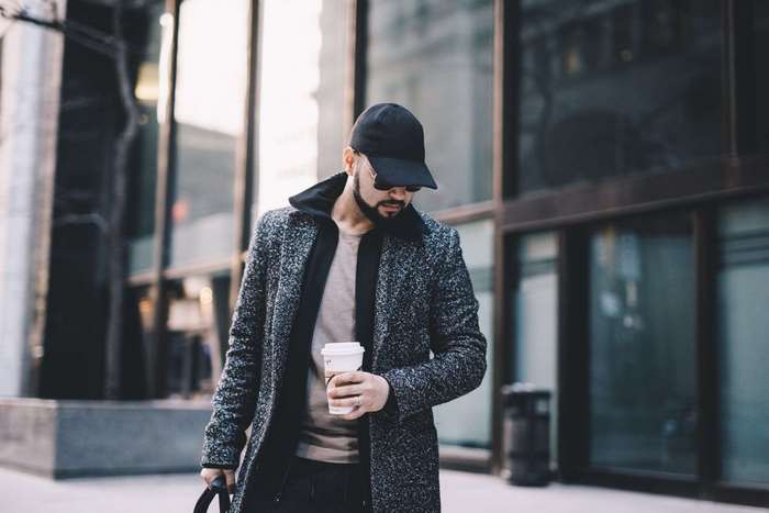Man in coat and cap holding coffee cup
