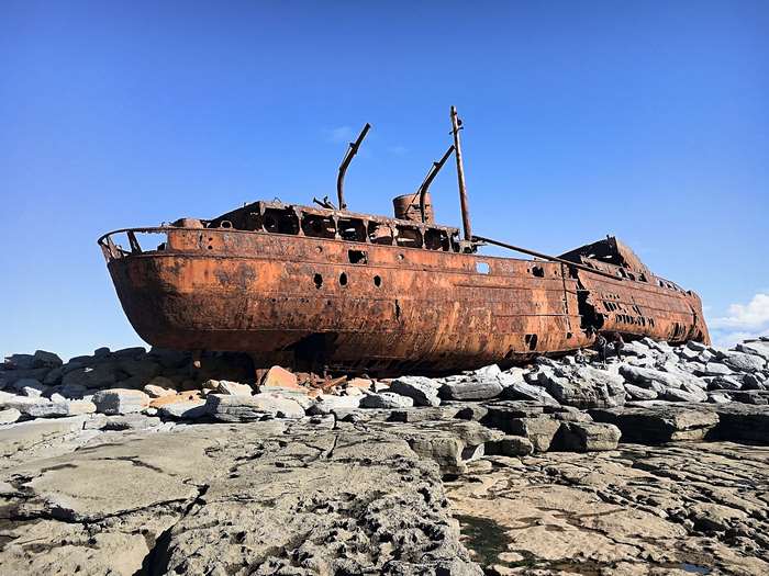 Rusty shipwreck on rocks under a clear blue sky