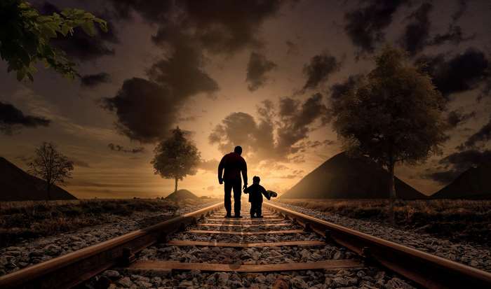 Father and son walking on train tracks at sunset
