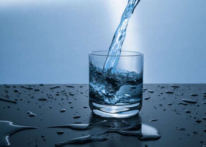 Water pouring into a glass on a wet surface