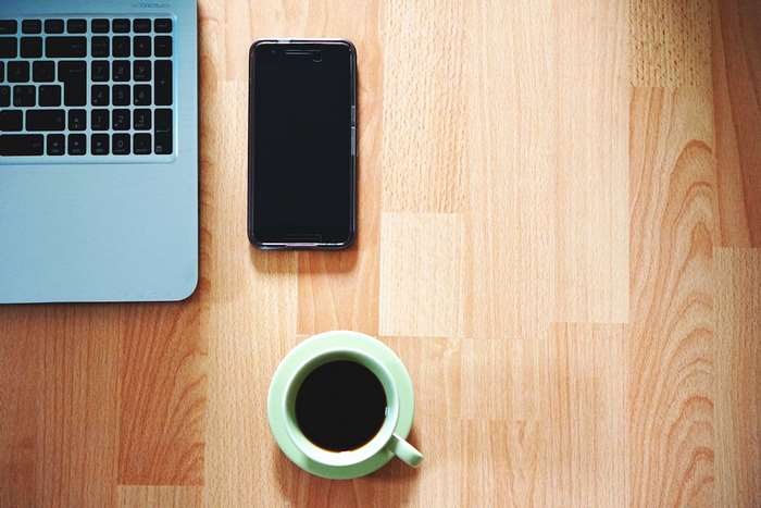 Laptop, smartphone, and coffee cup on a wooden desk