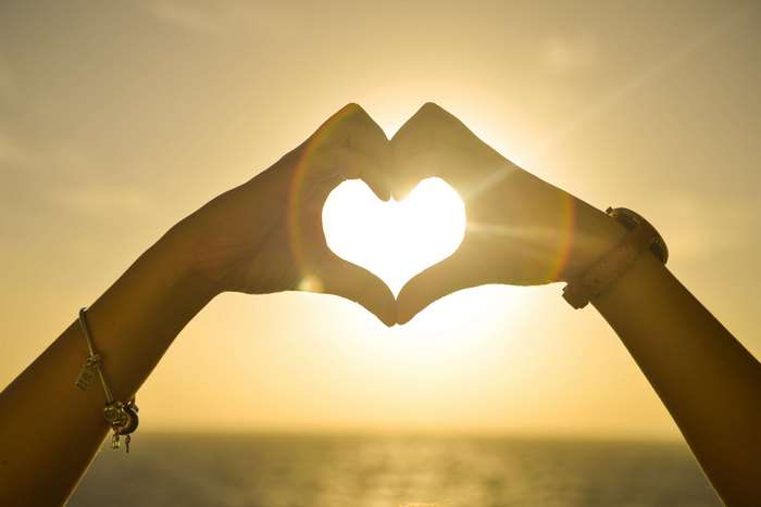 Hands forming a heart shape at sunset over the ocean