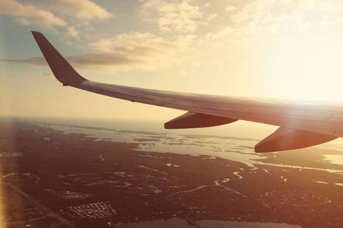Airplane wing flying over coastal landscape at sunset