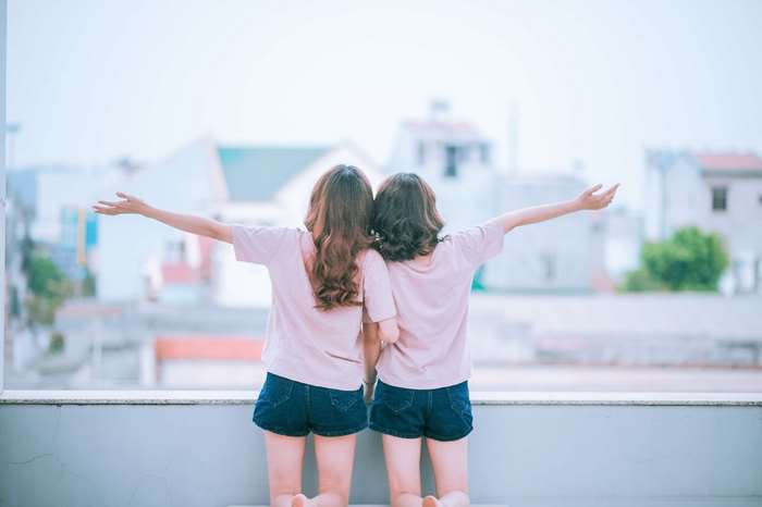 Two young women with arms outstretched on a balcony