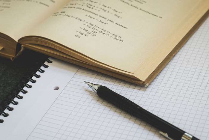 Open textbook with math equations and a pen on a notebook