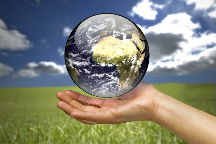 Hand holding the Earth globe over a grassy field