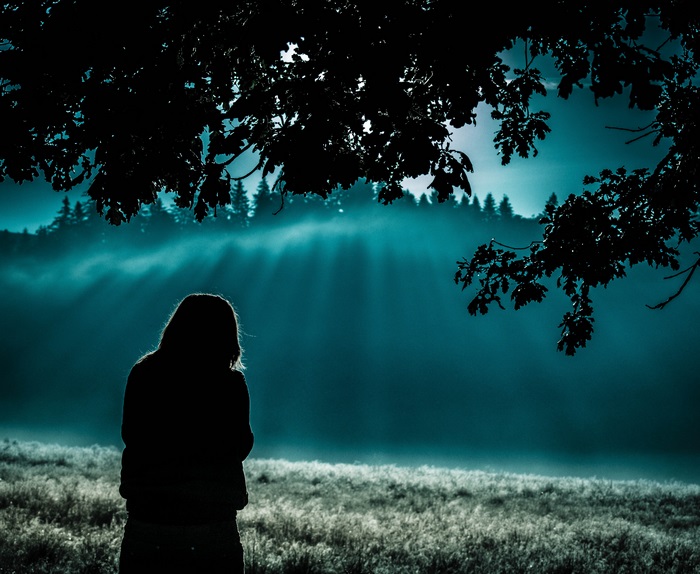 Girl silhouette in foggy forest with sun rays