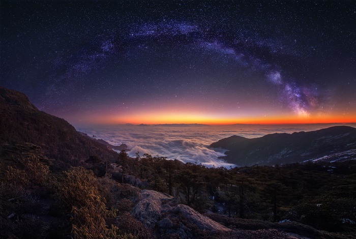 Milky Way over mountains and clouds at dawn