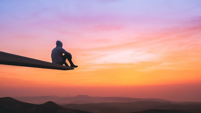 Person in hoodie sitting on wooden beam at sunset