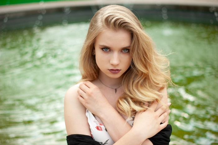 Blonde woman with green eyes in front of a fountain