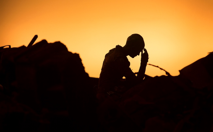 Silhouette of a person with hand on forehead against orange sky