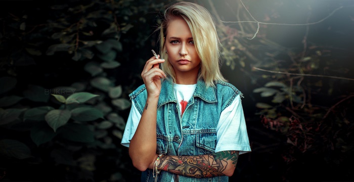 Woman with tattoos smoking a cigarette in a denim vest