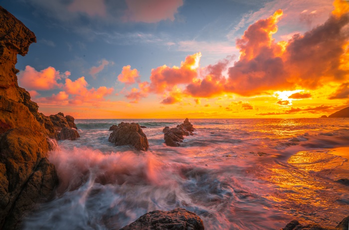 Sunset over the ocean with dramatic clouds and rocky shore