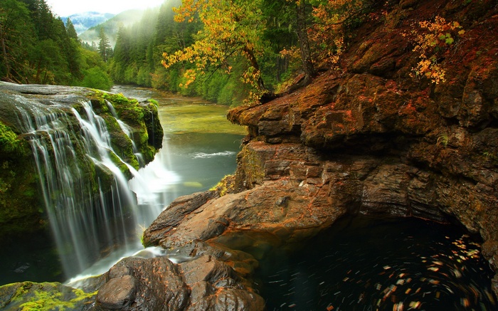 Waterfall cascading into a dark pool with autumn leaves