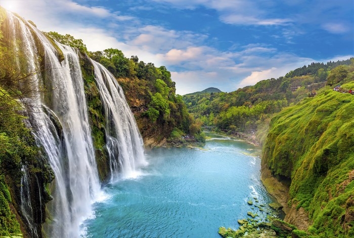 Waterfall cascading into a blue river surrounded by green mountains
