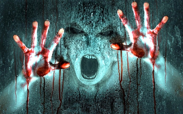 Scary face with bloody hands on wet glass