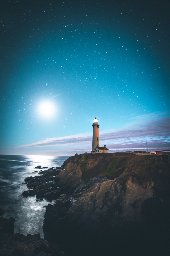 Lighthouse on a cliff under a starry sky with moon