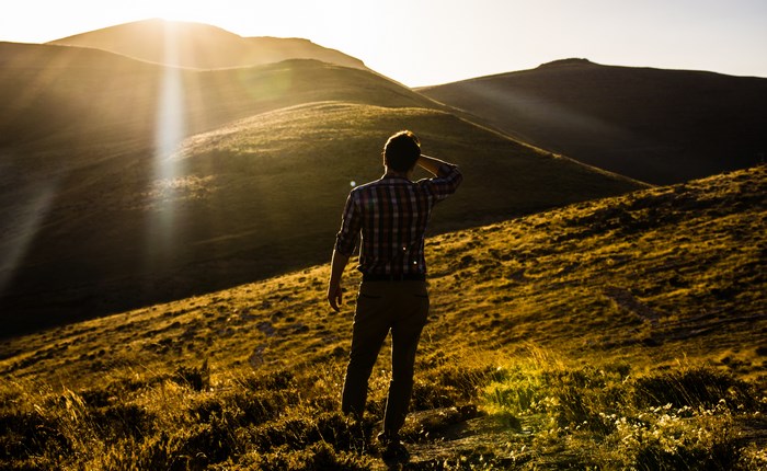 Man standing on a grassy hill at sunset