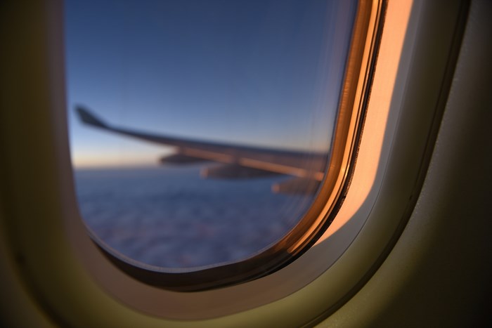 Airplane window view of wing at sunset over clouds