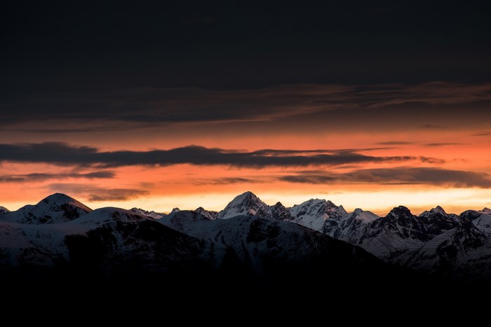 Snow-capped mountains at sunrise with orange clouds