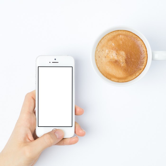 Hand holding iPhone with blank screen next to coffee cup