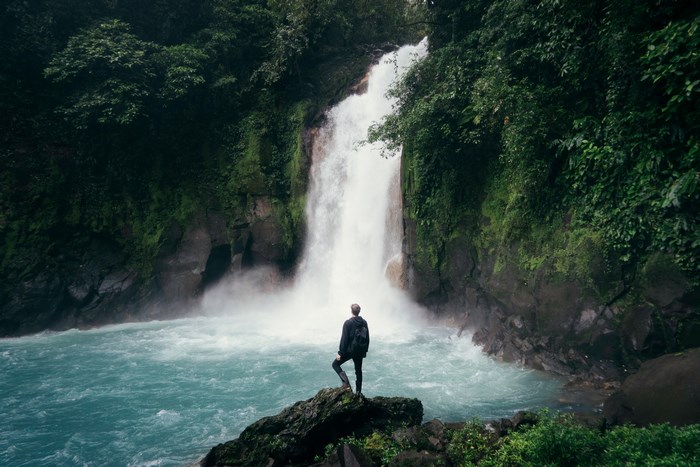 Man with backpack standing by a waterfall in a jungle