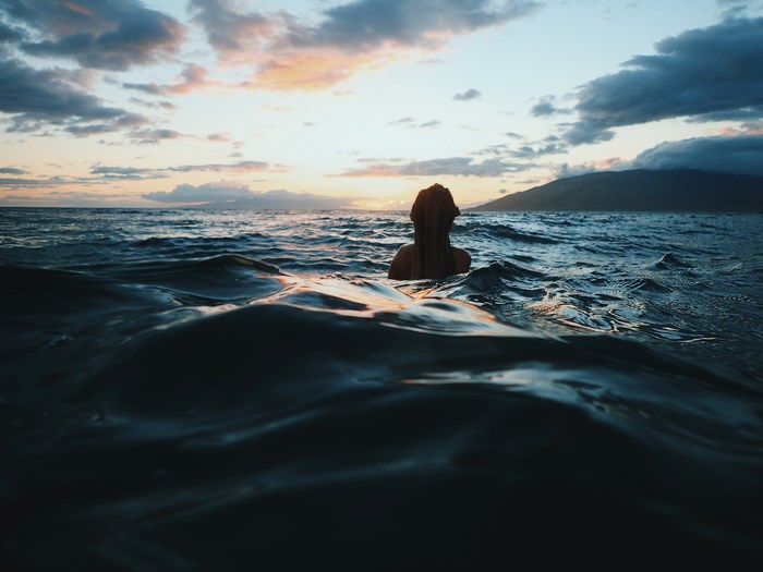 Woman swimming in ocean at sunset on Maui