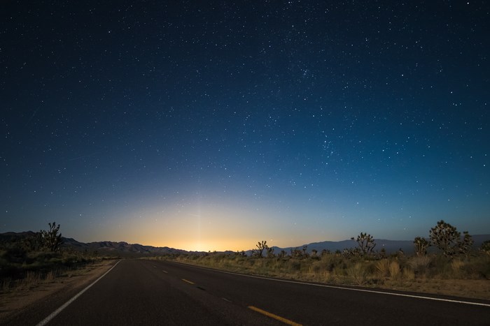 Desert road under a starry night sky with distant lights
